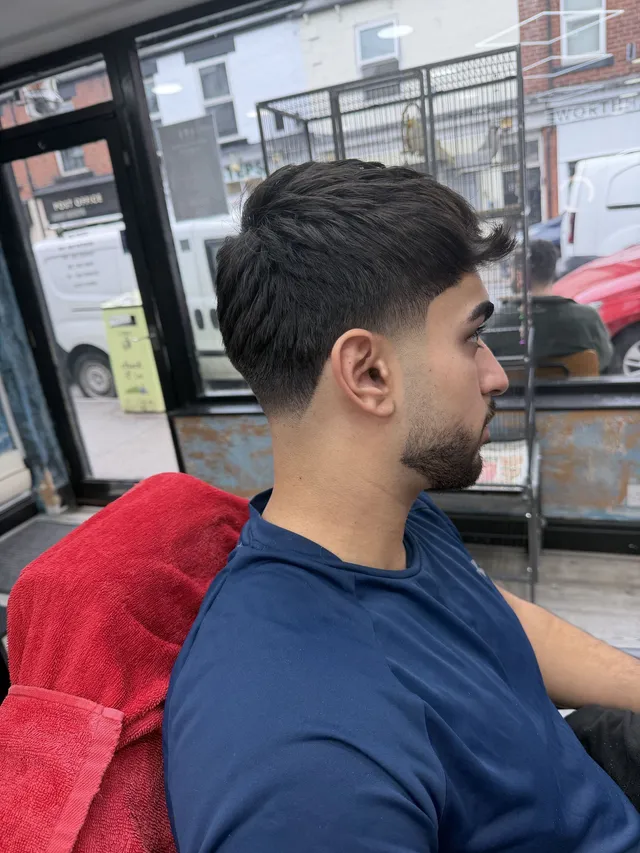 Side profile of a finished swept-back haircut and shaped beard by the shop window